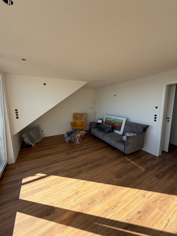 Een kamer met een houten vloer, een grijze bank, een gele fauteuil en een witte deur.