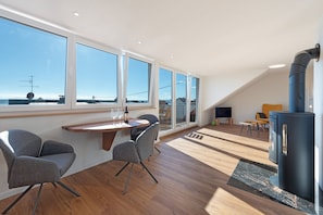 A modern interior with a dining area, a fireplace, and large windows offering a view of the sea.