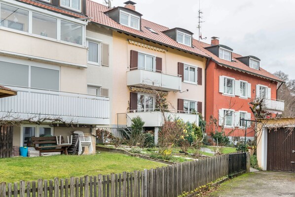 A row of residential buildings with balconies, a wooden fence, and a garden area.