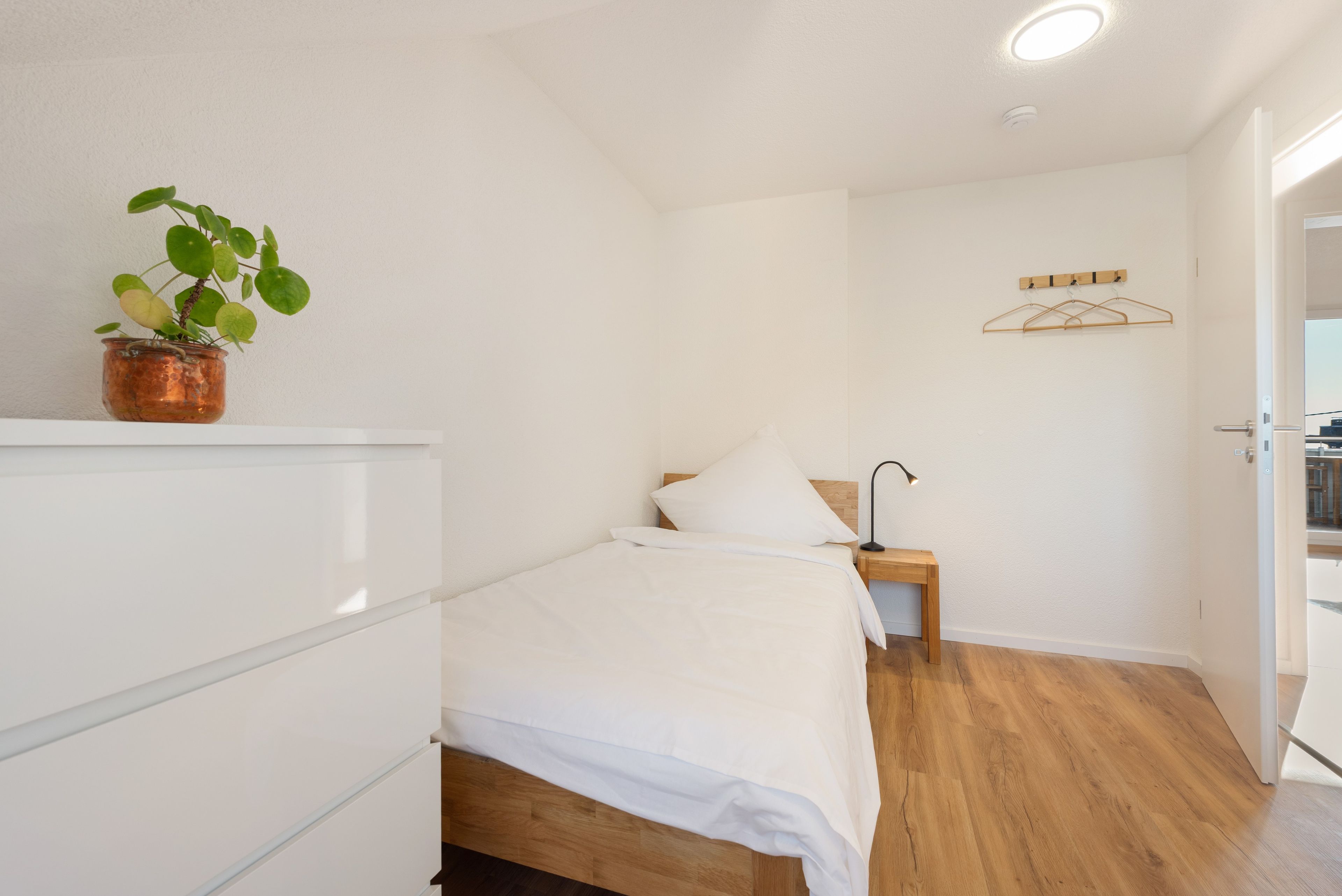 Une chambre à coucher avec un lit, une table de chevet, une lampe et une plante.