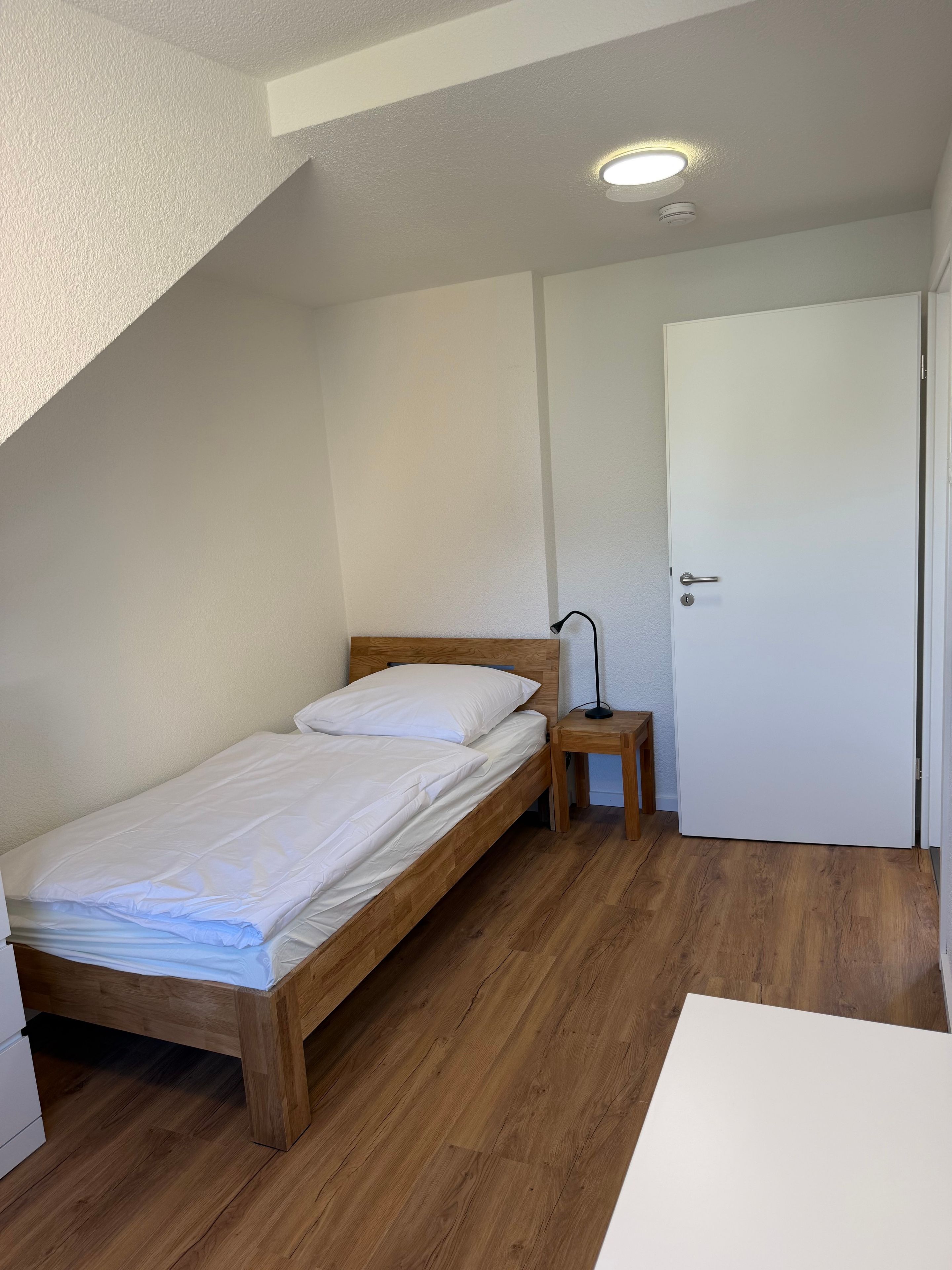 Ein Schlafzimmer mit einem hölzernen Bett, einem Nachttisch, einer Lampe und einer weißen Tür.