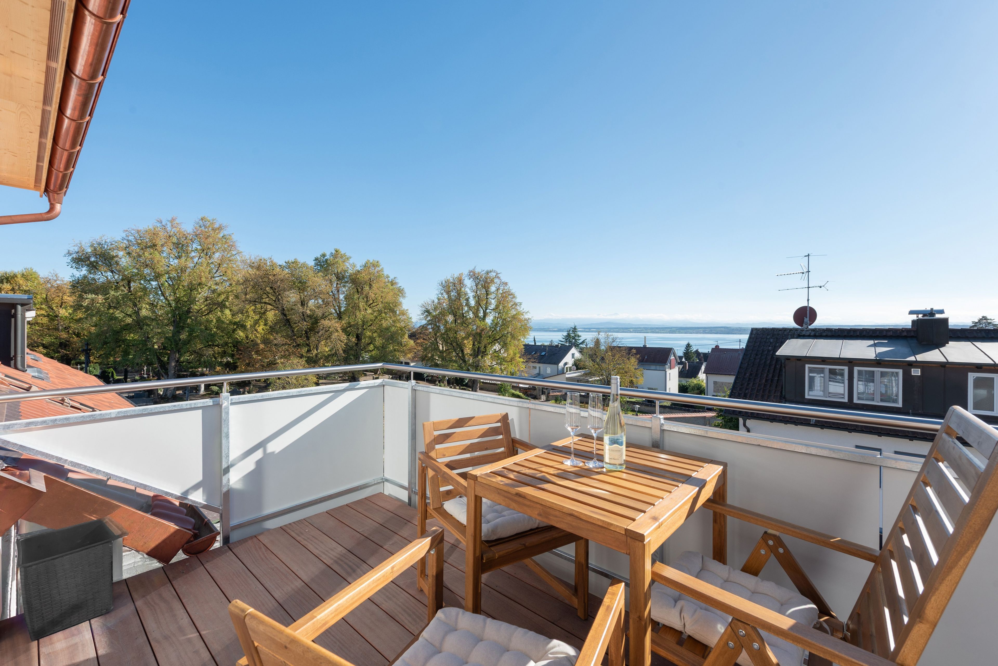 Eine Holzterrasse mit Tisch und Stühlen, mit Blick auf eine Stadtlandschaft und Bäume.