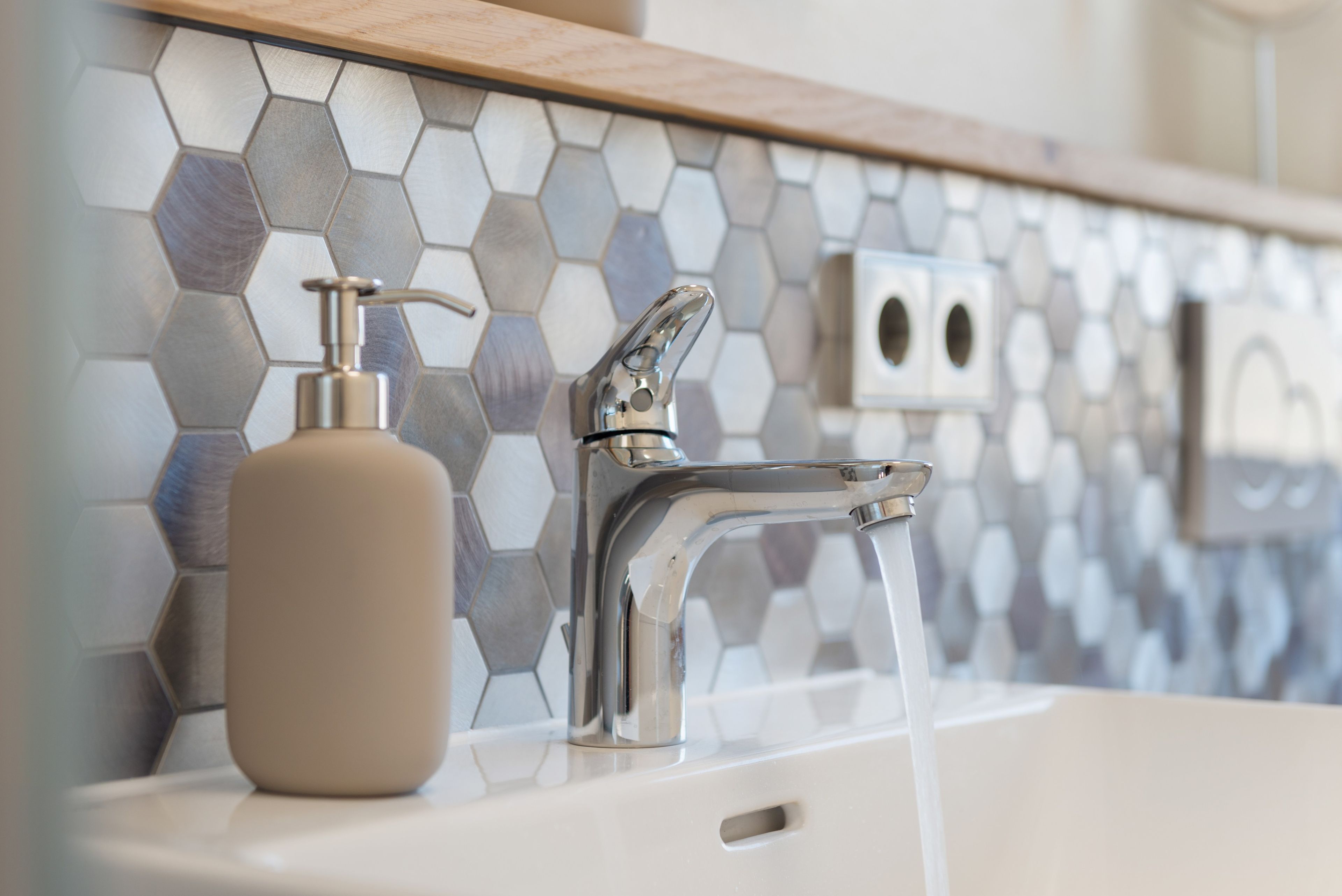 A bathroom with a modern faucet, a soap dispenser, and a hexagonal tile backsplash.