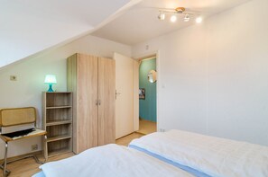 Una camera da letto con due letti, un armadio in legno, una sedia, una lampada e una porta che dà su un'altra stanza.