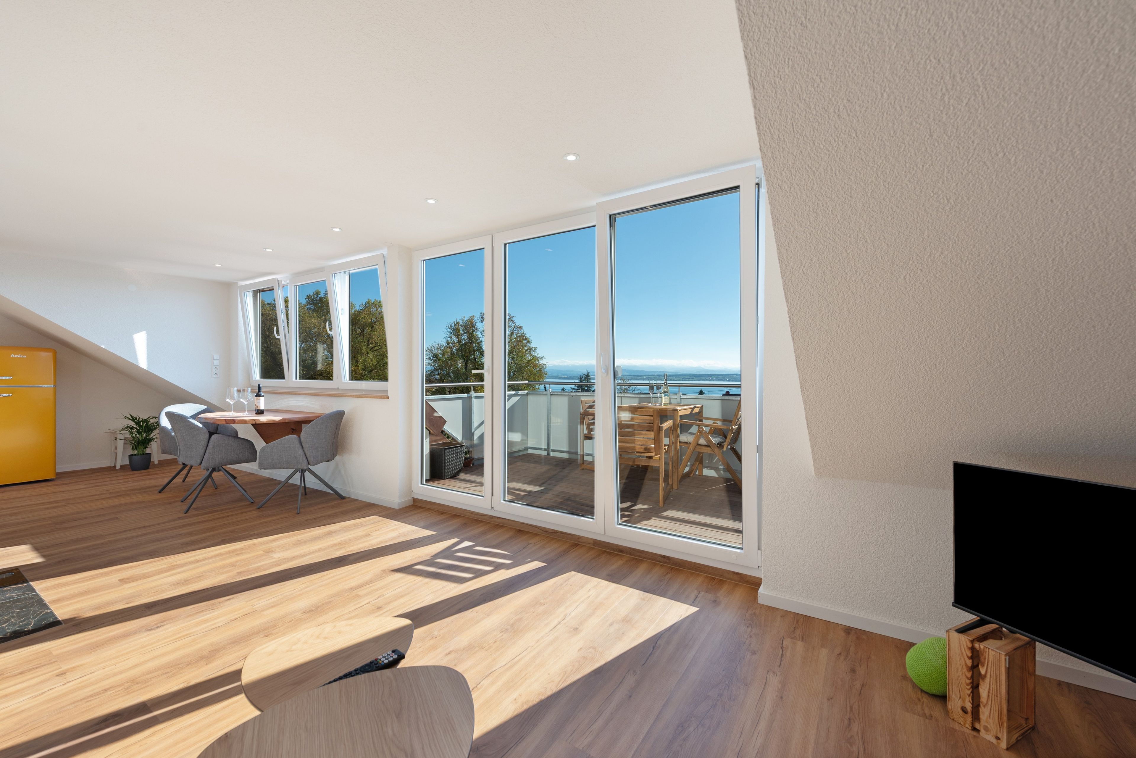 Ein modernes Wohnzimmer mit einem großen Schiebeglasfenster, das auf einen Balkon mit Meerblick führt.