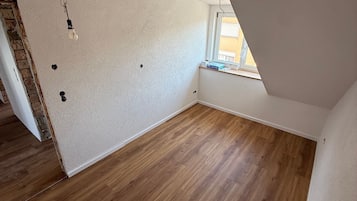 Een lege kamer met houten vloer, witte wanden en een schuin plafond.