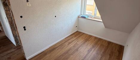 Une pièce vide avec un plancher en bois, des murs blancs et un plafond en pente.