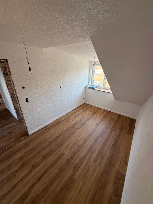 Une pièce vide avec un plancher en bois, des murs blancs et un plafond en pente.