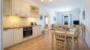 Een moderne keuken met witte kasten, een ingebouwde oven en een eethoek met een tafel en stoelen.