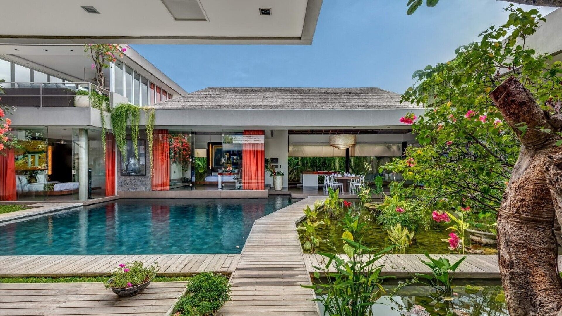 A modern hotel with a swimming pool, outdoor seating, and lush greenery.