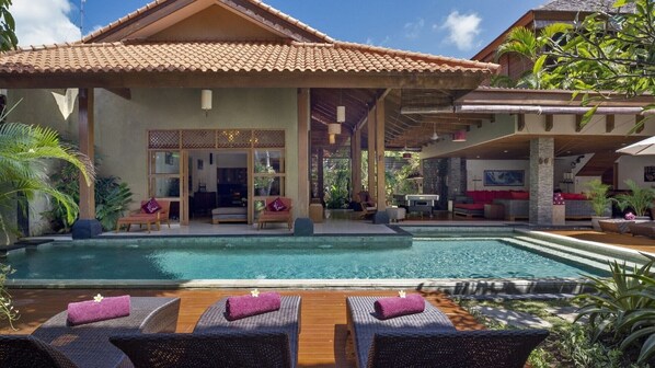 A resort with a swimming pool, lounge chairs, and a covered outdoor area with seating.