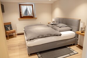 A bedroom with a bed, a nightstand, a lamp, a chair, a window with curtains, and a radiator. - Apartment 'Ferienwohnung Kasimir Hof' with Mountain View, Shared Garden and Wi-Fi (Seebach)