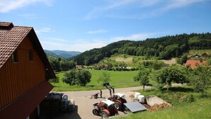 Paisagem rural com um celeiro vermelho, tratores estacionados e uma vista ampla das colinas e campos ao redor.