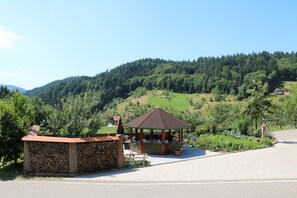 A gazebo with a tiled roof, surrounded by greenery and a stone wall.