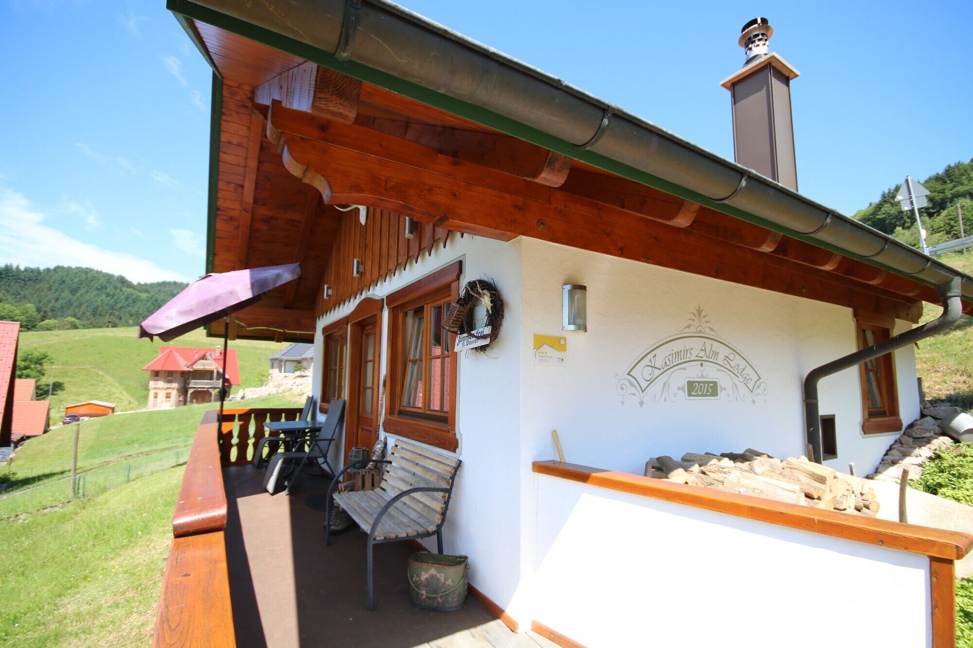 Ein Holzgebäude mit Veranda, einer Bank und einem Schild mit der Aufschrift 'Lásimir's Alm Lodge 2015'.