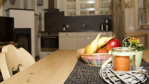 Una mesa de madera con un mantel tejido, una cesta de fruta, una vela y un tarro de cristal.
