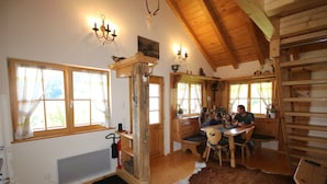 Un interior rústico con vigas de madera, una zona de comedor con alfombra de cuero de vaca y una chimenea.