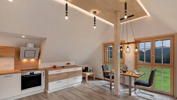 A modern kitchen with a built-in oven, wooden cabinets, and a dining area with a table and chairs. - Apartment 'Falkennest' with Mountain View, Shared Garden and Wi-Fi (Wolfach)