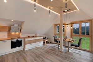 Una cocina moderna con horno empotrado, armarios de madera y una zona de comedor con mesa y sillas.