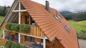 A wooden house with a sloped roof, a balcony with seating, and a view of a green landscape. - Apartment 'Falkennest' with Mountain View, Shared Garden and Wi-Fi (Wolfach)