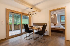 Une chambre moderne avec un plafond en bois, une table à manger avec des chaises, un lit avec une tête de lit et une vue à travers une porte vitrée.