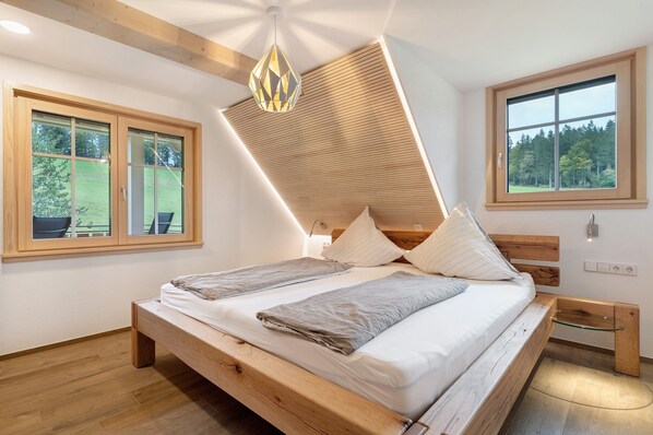 Une chambre à coucher avec un lit en bois, deux fenêtres, un puits de lumière et une vue sur l’extérieur.
