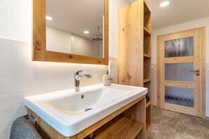 A bathroom with a white sink, wooden vanity, a mirror, and a frosted glass door.