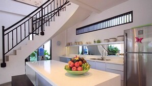 A modern kitchen with a white countertop, a stainless steel refrigerator, and a staircase with black railings.
