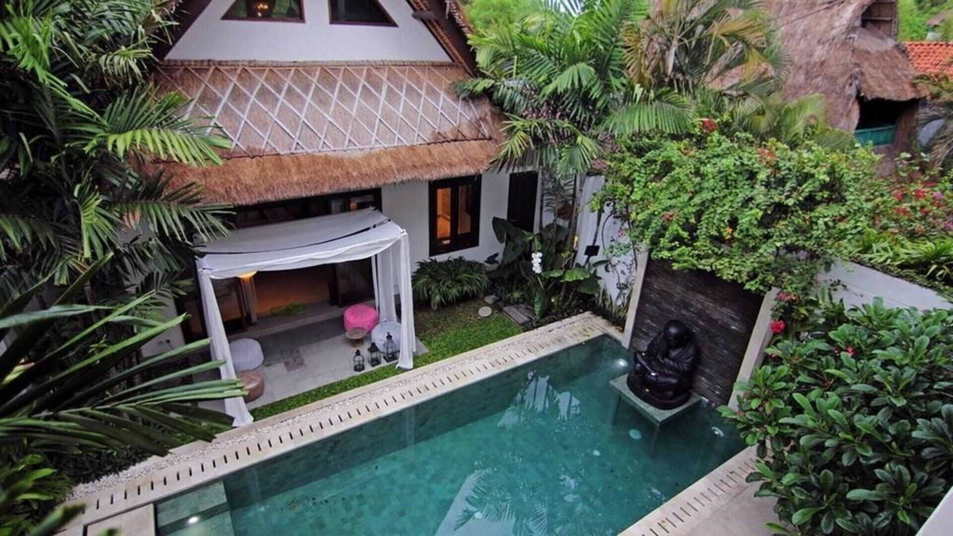 A pool area with a thatched-roof structure, a statue, and lush greenery.