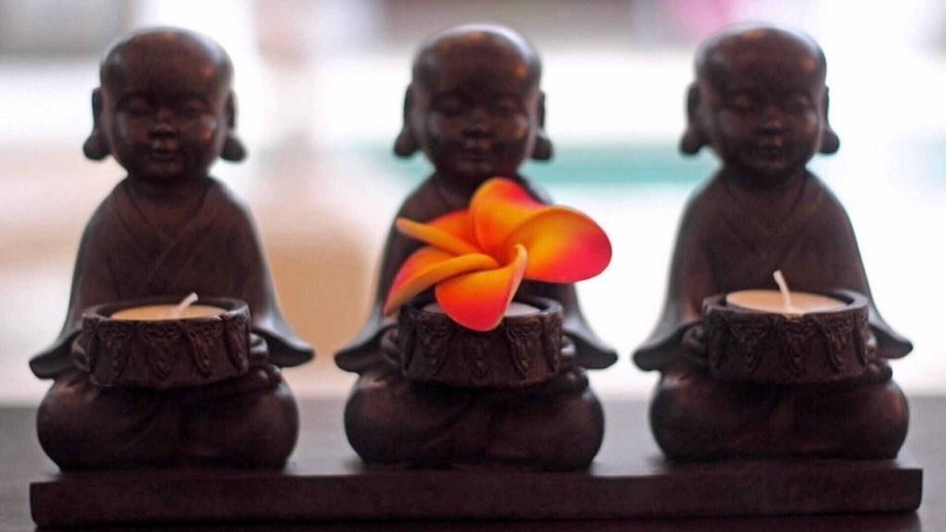 Three Buddha statues with candles and a flower in the center.