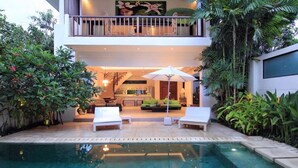 A modern outdoor pool area with lounge chairs, a dining area, and lush greenery.