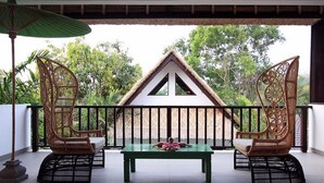 A balcony with wicker chairs, a table, and a thatched-roof structure in the background.