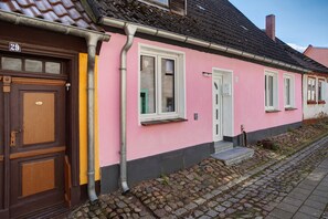 Um prédio rosa com porta marrom, numerado 29, e um pequeno alpendre com degraus.