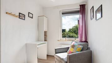 A small, bright room with a desk, chair, and window with curtains.