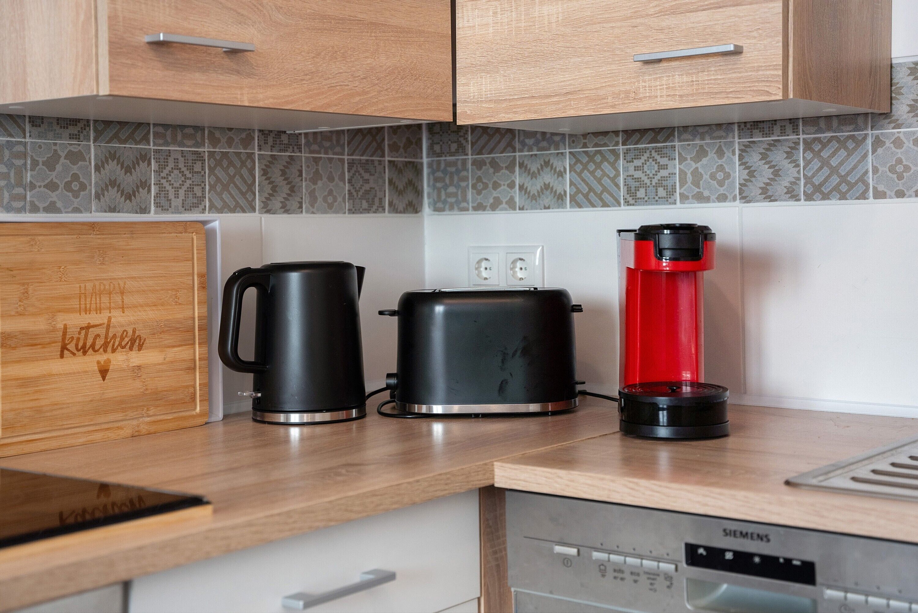 A kitchen with wooden cabinets, a coffee maker, a toaster, and a red coffee press on the countertop.