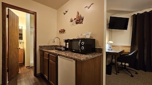 A compact kitchen with a microwave, coffee maker, and a small sink. There's a dining area with a table and a chair, and a TV mounted on the wall. - SIngle Executive Suite (Laurium)