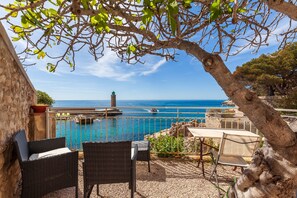 A terrace with wicker furniture, a table, and chairs overlooking a pool and the sea.