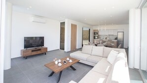 A modern living room with a sofa, coffee table, TV, and a kitchen in the background.