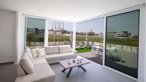 A modern living room with a large sofa, a coffee table, and a balcony with outdoor seating and a view of the cityscape.