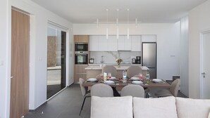 A modern kitchen with white cabinets, a dining table set for six, and a sofa in the foreground.