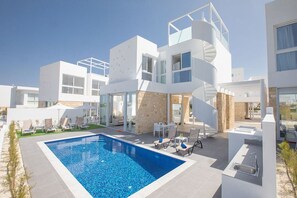 A modern multi-story building with a swimming pool, outdoor seating, and a stone facade. - 5 Star Private Villa at Best Rate, Protaras Villa 1715 (Protaras)
