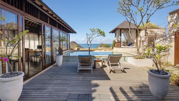A wooden deck with two lounge chairs, a small table, and a glass-enclosed room with a view of the sea. - Peaceful 16BR Villa W/ Pool in Bali, Bali Villa 2209 (Bali)
