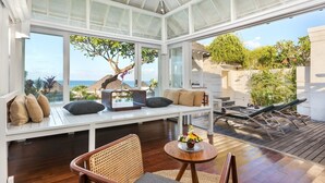 Een moderne, open woonkamer met uitzicht op zee, een houten terras en een glazen patio.