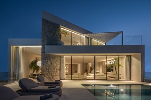 Una casa moderna con un espacio de estar con paredes de vidrio, piscina y un muro de piedra.