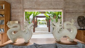 A room with two white dragon sculptures on pedestals, a wooden bookshelf, and a view of a pool and garden through an open doorway.