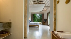A modern bedroom with a large bed, a TV, and a view of greenery outside.