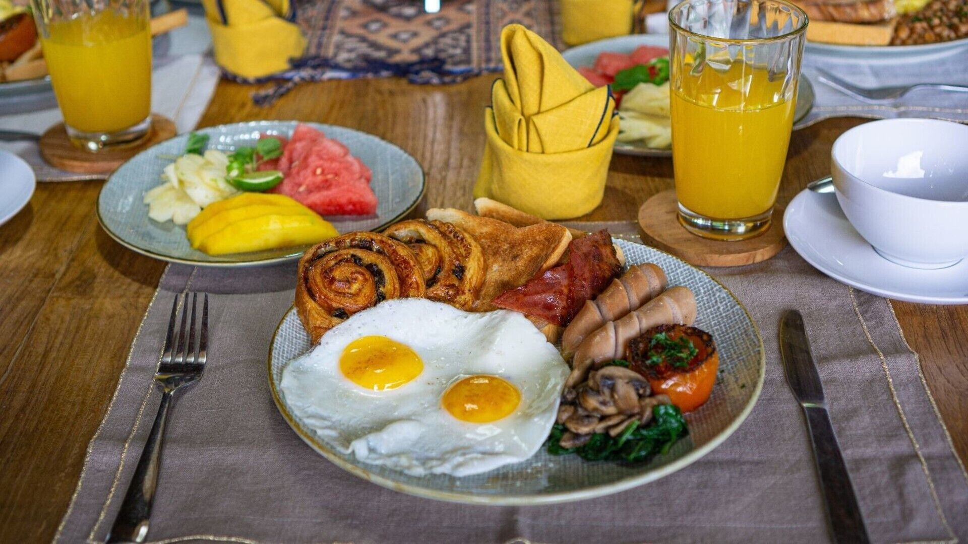 Desayuno con platos de huevos, tocino, champiñones y tostadas, acompañado de un vaso de jugo de naranja.