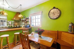 A kitchen with a green wall, wooden bar stools, a wooden table, and a clock.