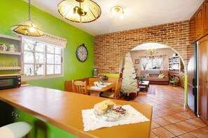 A kitchen with a dining table, chairs, a refrigerator, and a clock on the wall.