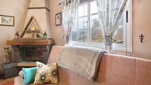 Ein gemütliches Wohnzimmer mit Kamin, einer Couch mit Decke und einem Fenster mit Vorhängen.